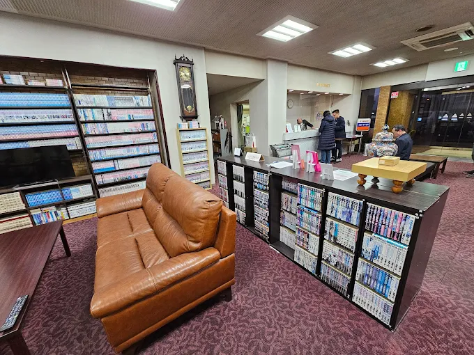 Business Hotel Pocket — cozy lobby lounge featuring an extensive manga library with floor-to-ceiling bookshelves and comfortable leather seating for guests in Matsushige, Tokushima. | Hotel Manga