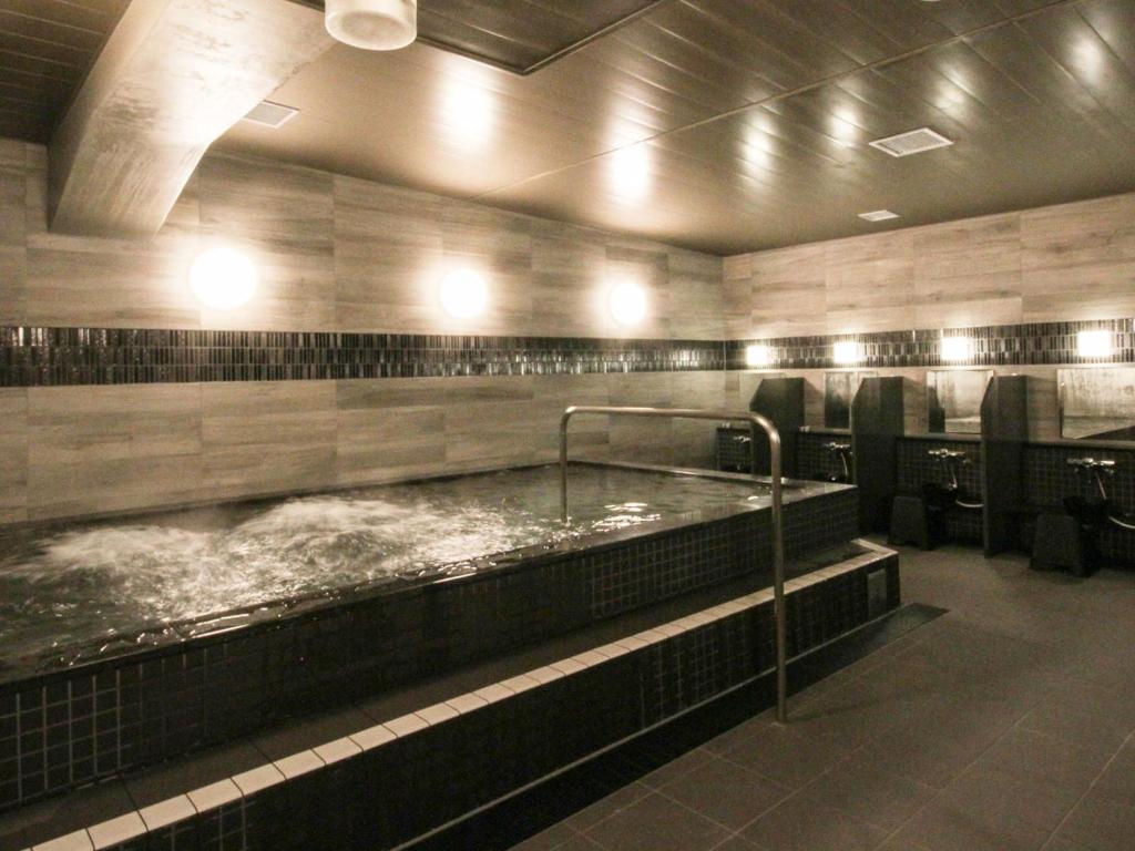 Grancustoma Ueno - Modern communal hot bath (sento-style) with a jacuzzi feature and adjacent washing stations, Tokyo.