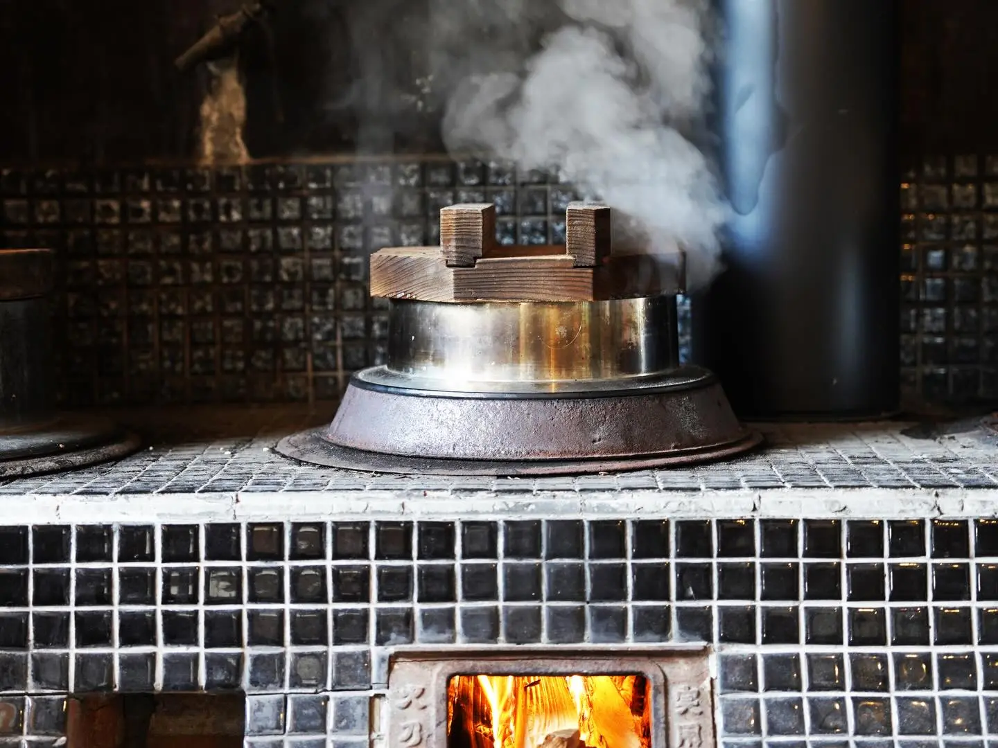 Irori hearth dinner at Magokoro — open kitchen with chef cooking gibier, river fish and gohei-mochi over open fire, smoke-blackened beams above