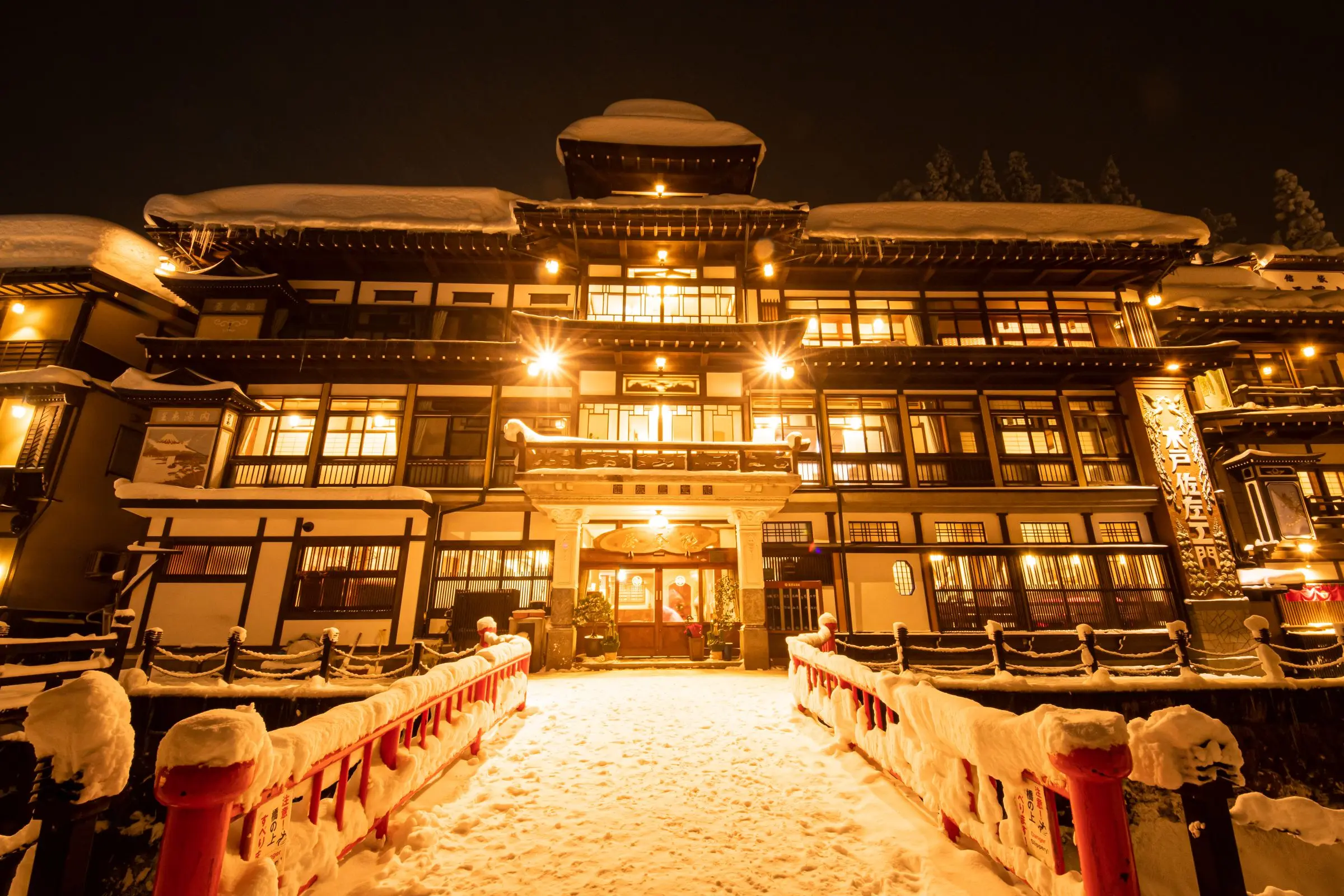 Notoya Ryokan at night in winter — Taisho-era wooden four-storey building glowing on the gas-lit Ginzan River street, Ginzan Onsen Yamagata