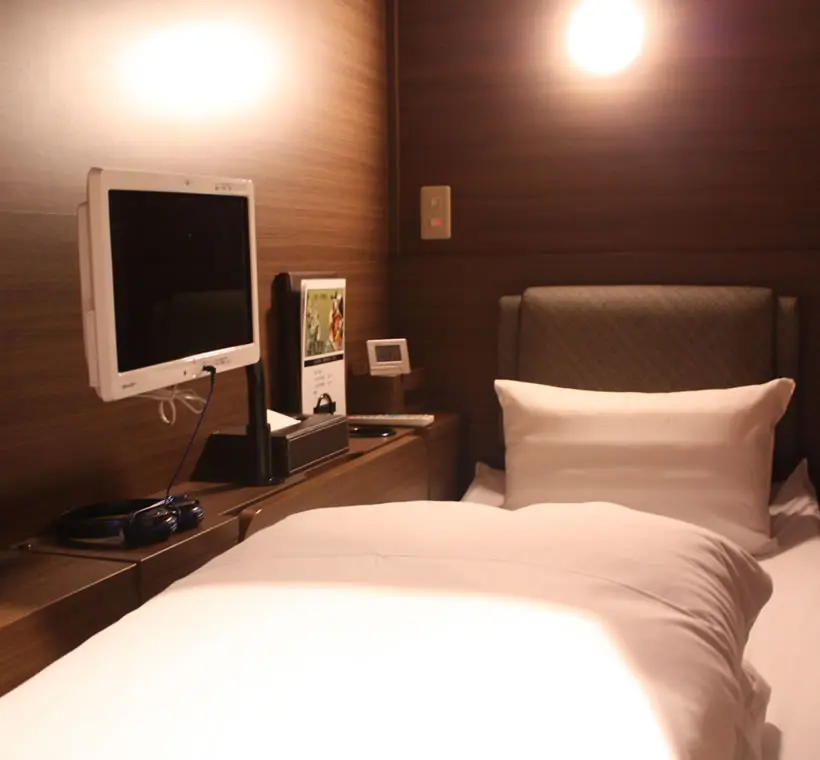 Teriha Spa Resort 照葉スパリゾート — private cabin room featuring a compact bed, personal monitor, and wood-paneled walls for overnight stays in Fukuoka. | Hotel Manga